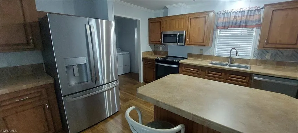 Kitchen featuring appliances with stainless steel finishes, brown cabinetry, light countertops, and crown molding