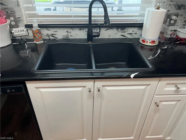 Interior details featuring black dishwasher, white cabinetry, and sink