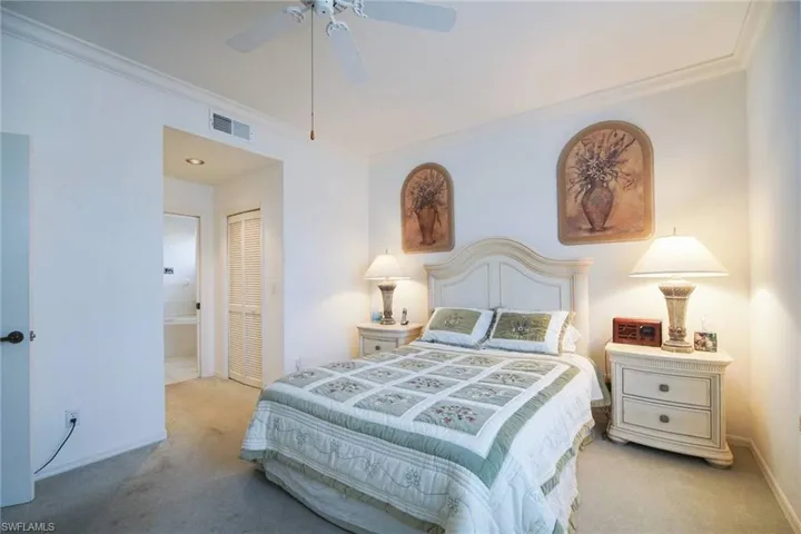 Carpeted bedroom with ornamental molding, two closets, ceiling fan, and ensuite bath