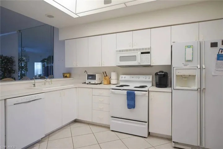 Kitchen featuring white cabinets, white appliances, light tile patterned floors, and sink