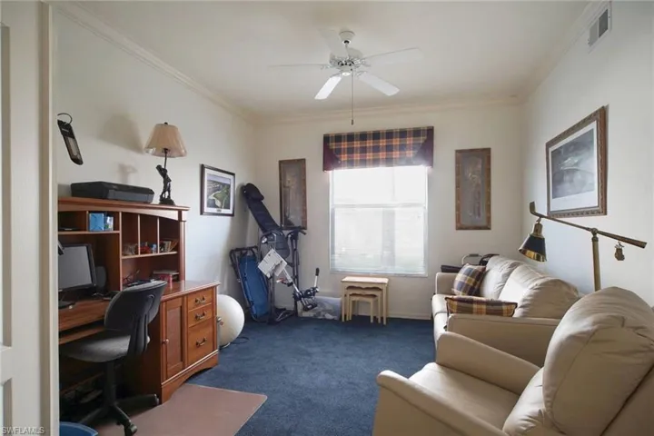 Carpeted home office with ceiling fan and ornamental molding