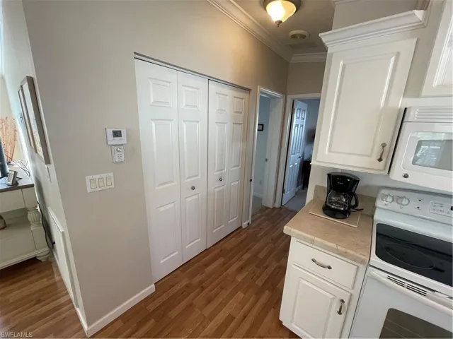 Kitchen with range, white microwave, light countertops, white cabinets, and dark wood-type flooring