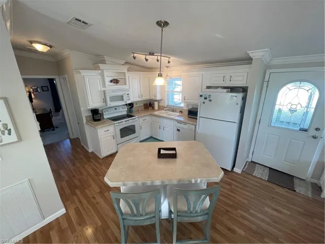Kitchen featuring ornamental molding, white appliances, white cabinets, light countertops, and a kitchen bar