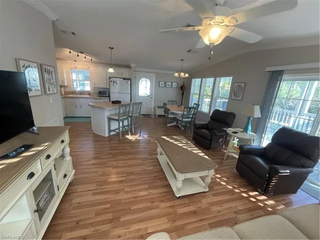 Living area with crown molding, vaulted ceiling, light wood-style flooring, a ceiling fan, and suspended lighting