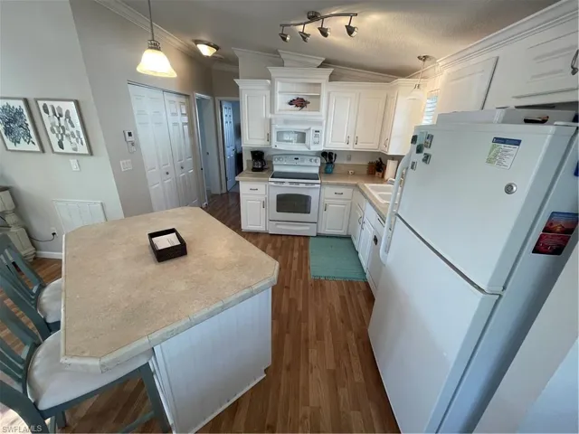 Kitchen with fridge, white range oven, white cabinets, dark wood-style flooring, and ornamental molding