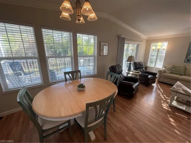 Dining space featuring a chandelier, vaulted ceiling, ornamental molding, and dark wood finished floors