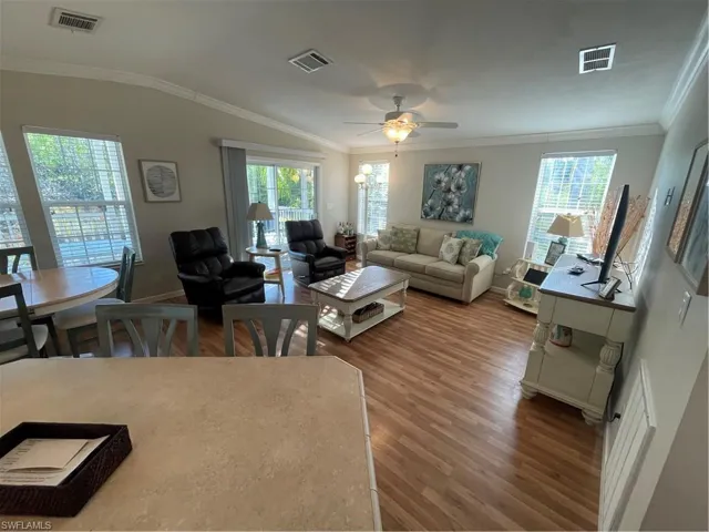 Living room featuring ceiling fan, crown molding, dark wood-type flooring, lofted ceiling, and healthy amount of natural light