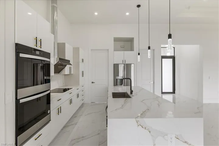 Kitchen featuring decorative light fixtures, marble finish floor, white cabinetry, stainless steel refrigerator with ice dispenser, and a sink