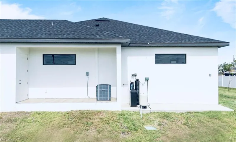 Rear view of house featuring central air condition unit, a shingled roof, a lawn, and stucco siding
