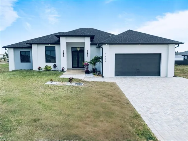 Prairie-style house with an attached garage, stucco siding, decorative driveway, and a front yard