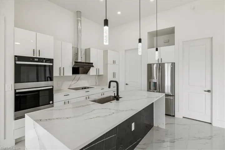 Kitchen featuring white cabinets, a center island quartz countertop with sink, pendant lighting, and stainless steel appliances