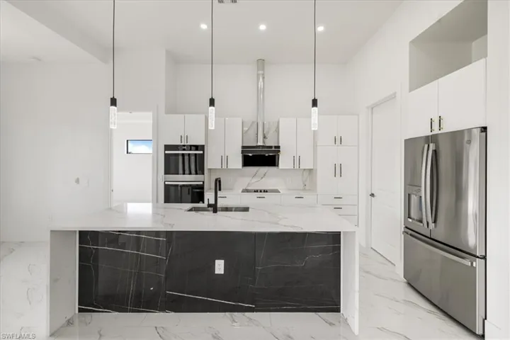 Kitchen featuring light stone counters, decorative light fixtures, stainless steel appliances, white cabinets, and a sink