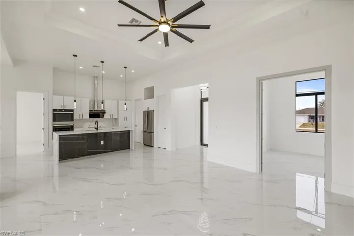 Great Room/Kitchen featuring pendant lighting, light countertops, appliances with stainless steel finishes, white cabinets, and an island with sink