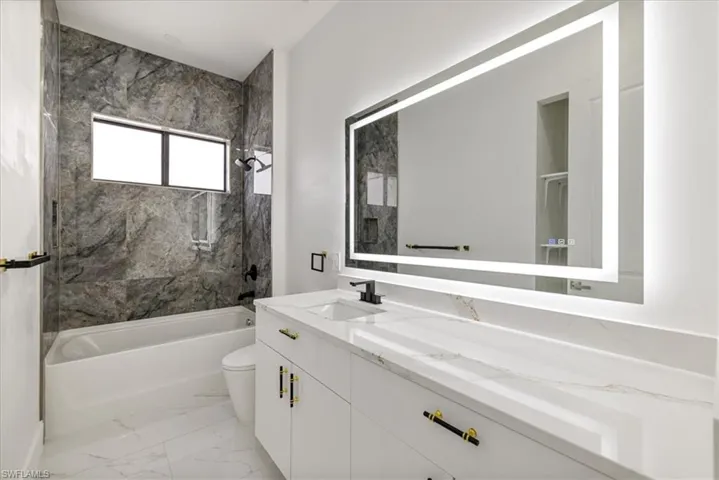 Full n.2 Guess bath featuring double vanity, toilet, marble finish floor, a sink, and shower / bathing tub combination