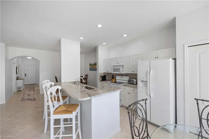 Kitchen with white appliances, backsplash, white cabinets, sink, and light stone countertops