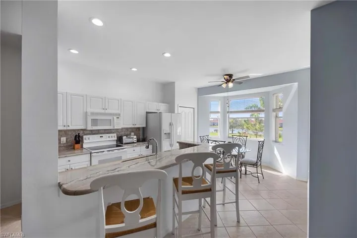 Kitchen featuring white cabinetry, light stone counters, white appliances, a kitchen bar, and decorative backsplash