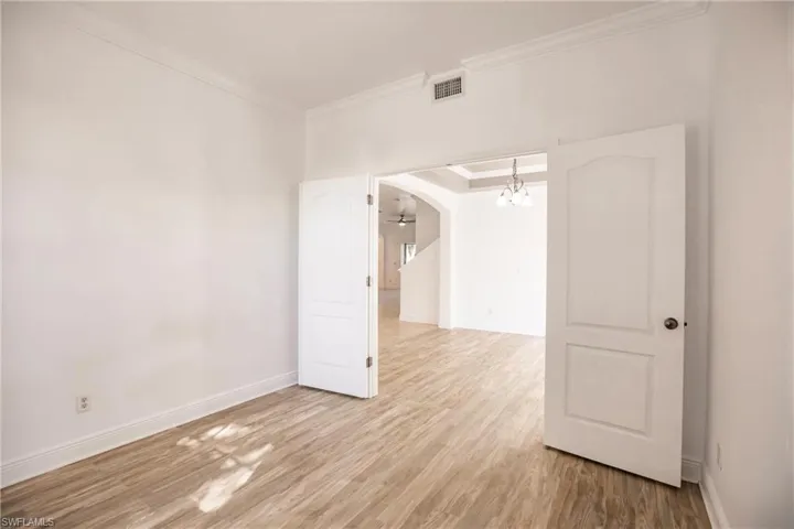 Empty room with crown molding, light hardwood / wood-style flooring, and a notable chandelier