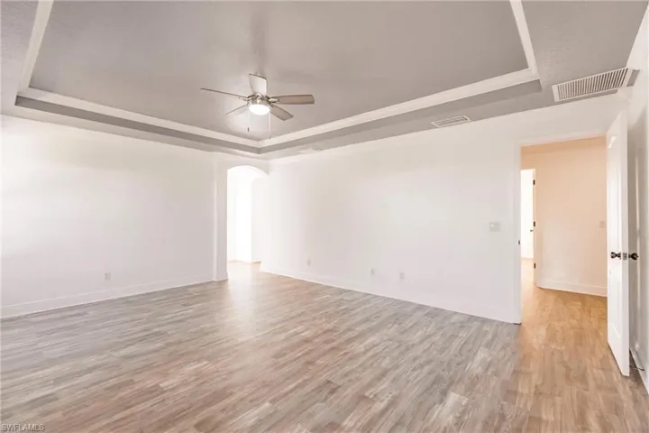 Spare room featuring a raised ceiling, ceiling fan, and light wood-type flooring