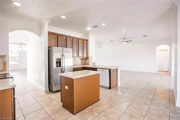 Kitchen with dishwasher, ceiling fan with notable chandelier, stainless steel fridge, light tile patterned flooring, and kitchen peninsula