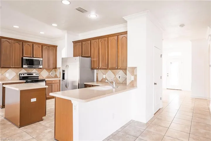 Kitchen with kitchen peninsula, appliances with stainless steel finishes, sink, light tile patterned floors, and a center island