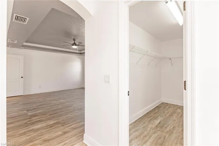 Spacious closet with ceiling fan, light hardwood / wood-style floors, and a tray ceiling