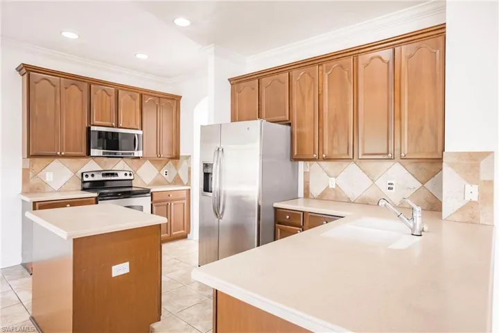 Kitchen featuring decorative backsplash, appliances with stainless steel finishes, crown molding, sink, and light tile patterned floors