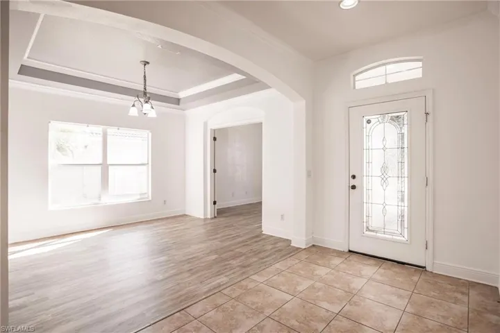Entrance foyer with light hardwood / wood-style floors, a healthy amount of sunlight, ornamental molding, and a tray ceiling