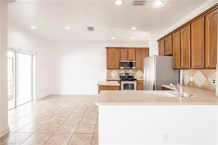 Kitchen with sink, ornamental molding, appliances with stainless steel finishes, light tile patterned flooring, and kitchen peninsula