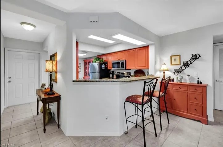 Kitchen with a peninsula, light tile patterned flooring, stone counters, baseboards, and appliances with stainless steel finishes