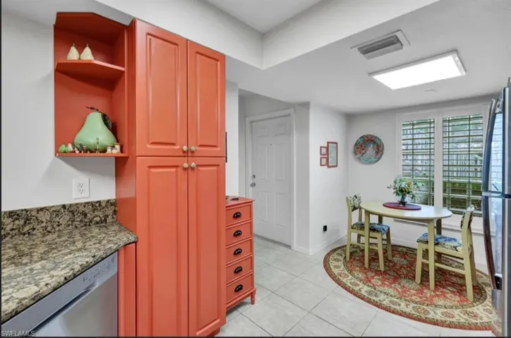 Kitchen featuring dark stone countertops, open shelves, light tile patterned flooring, stainless steel appliances, and visible vents