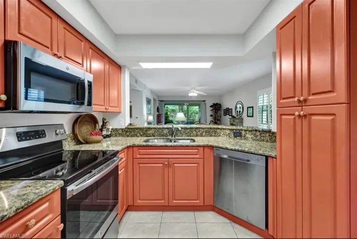 Kitchen featuring a peninsula, a sink, appliances with stainless steel finishes, light stone counters, and light tile patterned floors