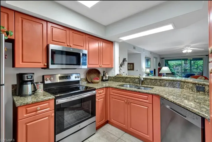 Kitchen featuring a sink, light tile patterned floors, stone counters, a peninsula, and appliances with stainless steel finishes
