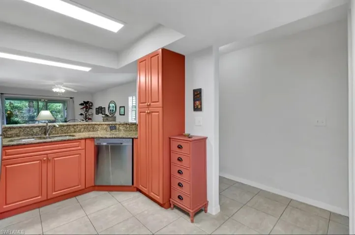 Kitchen with dark stone counters, stainless steel dishwasher, a sink, light tile patterned floors, and baseboards
