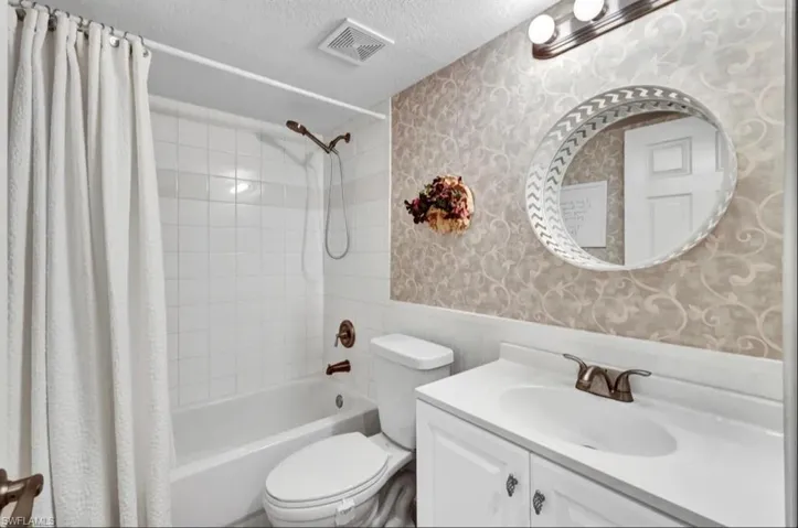 Full bath featuring shower / bath combo, a textured ceiling, wallpapered walls, a wainscoted wall, and visible vents