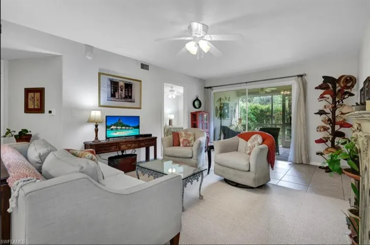 Carpeted living room with tile patterned flooring, visible vents, and a ceiling fan