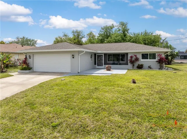 Single story home featuring concrete driveway, stucco siding, a front lawn, a fire pit, and a garage