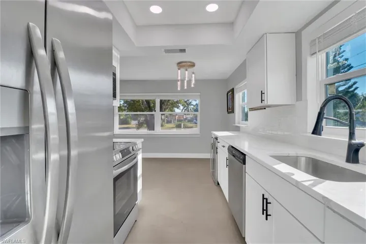 Kitchen featuring stainless steel appliances, white cabinets, light stone countertops, recessed lighting, and plenty of natural light