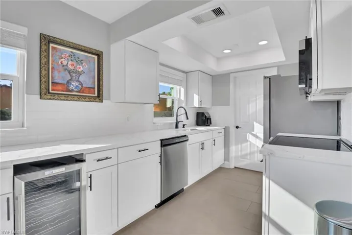 Kitchen featuring wine cooler, decorative backsplash, white cabinetry, light stone countertops, and recessed lighting