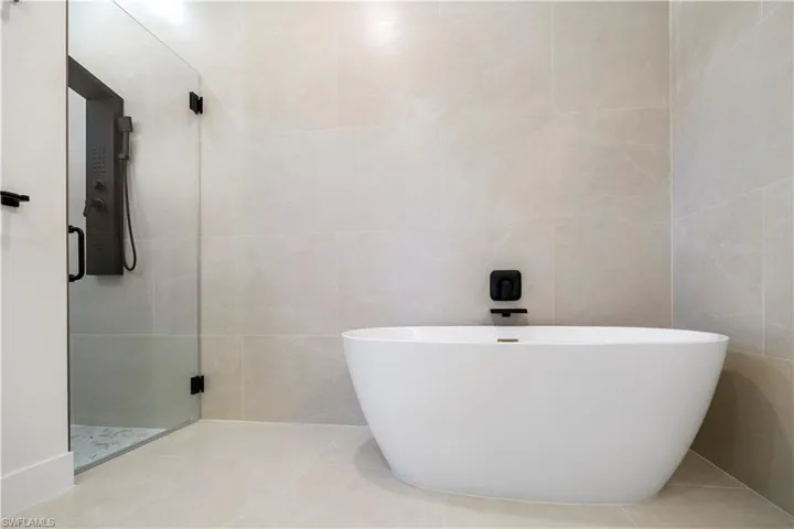 Bathroom featuring a shower stall, tile walls, a soaking tub, and tile patterned flooring
