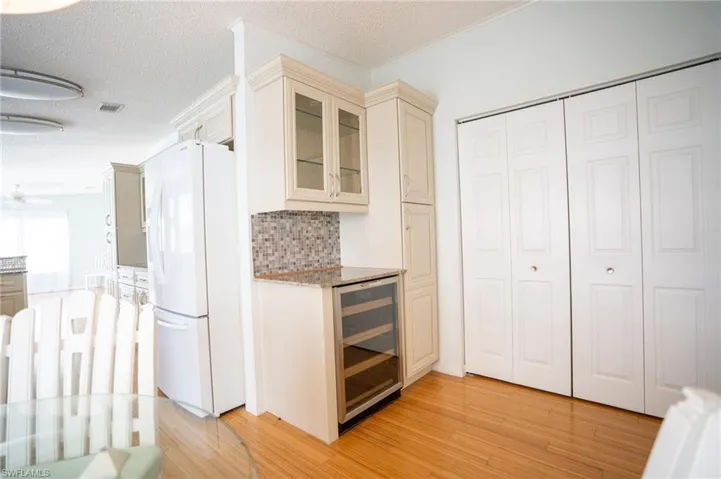 Bar area featuring freestanding refrigerator, wine cooler, light wood-style floors, decorative backsplash, and ornamental molding