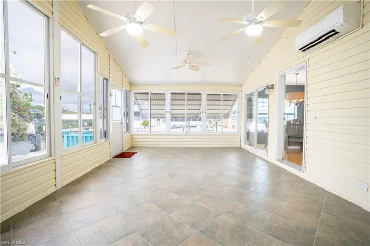 Unfurnished sunroom with a wall mounted AC, ceiling fan, vaulted ceiling, and plenty of natural light