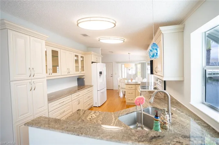 Kitchen featuring white appliances, a textured ceiling, plenty of natural light, glass insert cabinets, and light stone counters