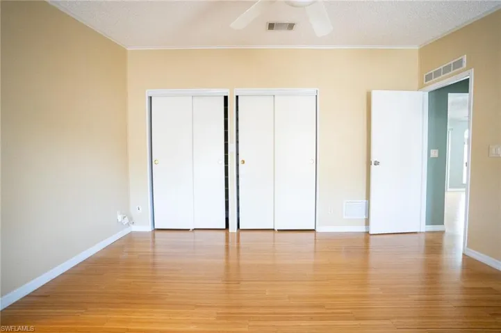 Unfurnished bedroom featuring ornamental molding, two closets, light wood-style floors, and a ceiling fan