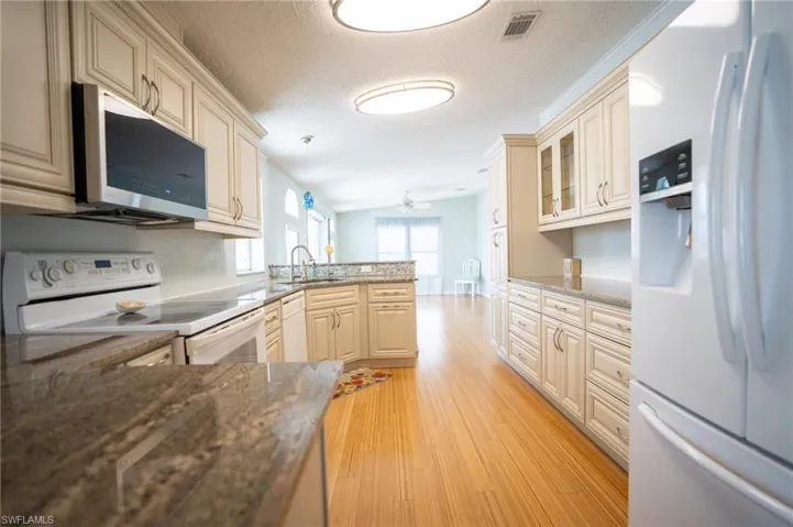 Kitchen with white appliances, a peninsula, light wood finished floors, glass insert cabinets, and a ceiling fan