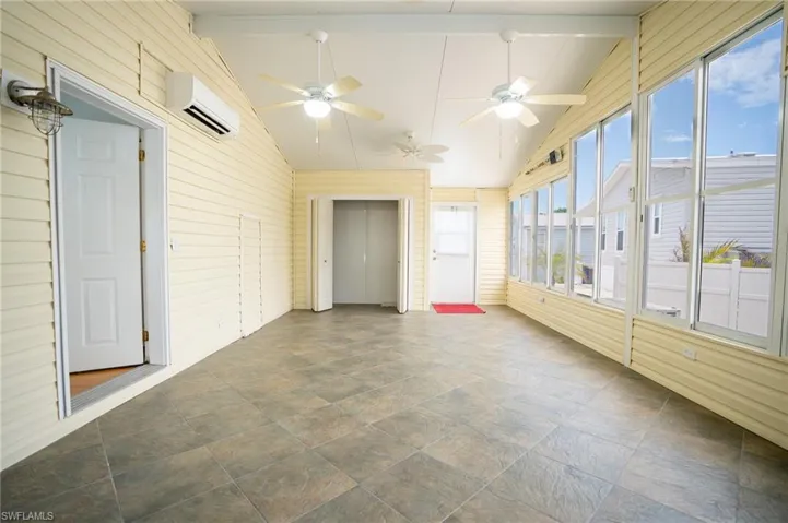 Unfurnished sunroom featuring a wall unit AC, ceiling fan, wooden walls, and stone finish floors