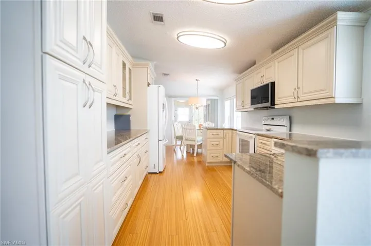 Kitchen featuring white appliances, light wood finished floors, decorative light fixtures, glass insert cabinets, and a textured ceiling