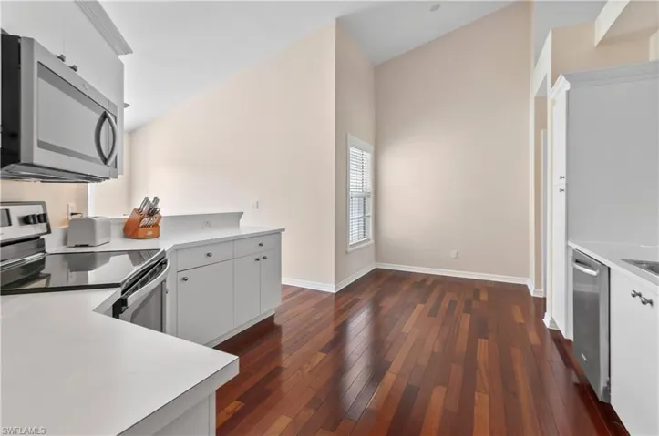 Kitchen featuring stainless steel appliances, light countertops, white cabinetry, dark wood-style flooring, and lofted ceiling