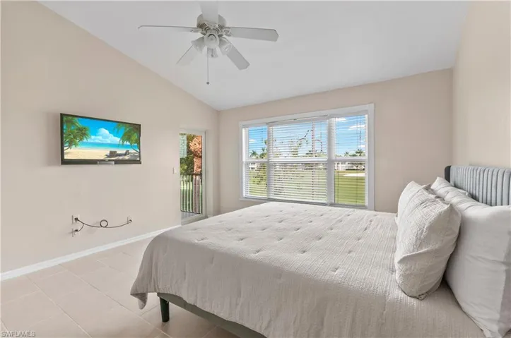 Tiled bedroom featuring vaulted ceiling, access to exterior, and ceiling fan