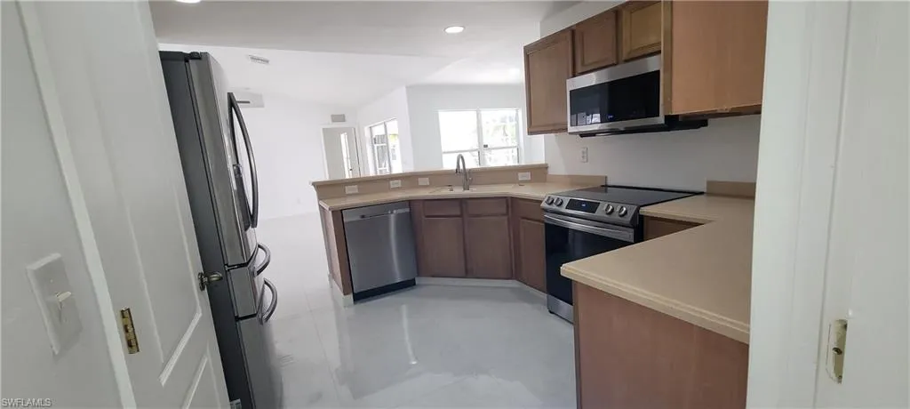 Kitchen featuring stainless steel appliances, a peninsula, light countertops, recessed lighting, and wood finish cabinets