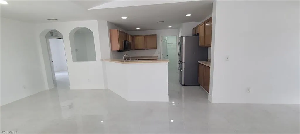 Kitchen with arched walkways, stainless steel appliances, wood finish cabinetry, recessed lighting, and light countertops